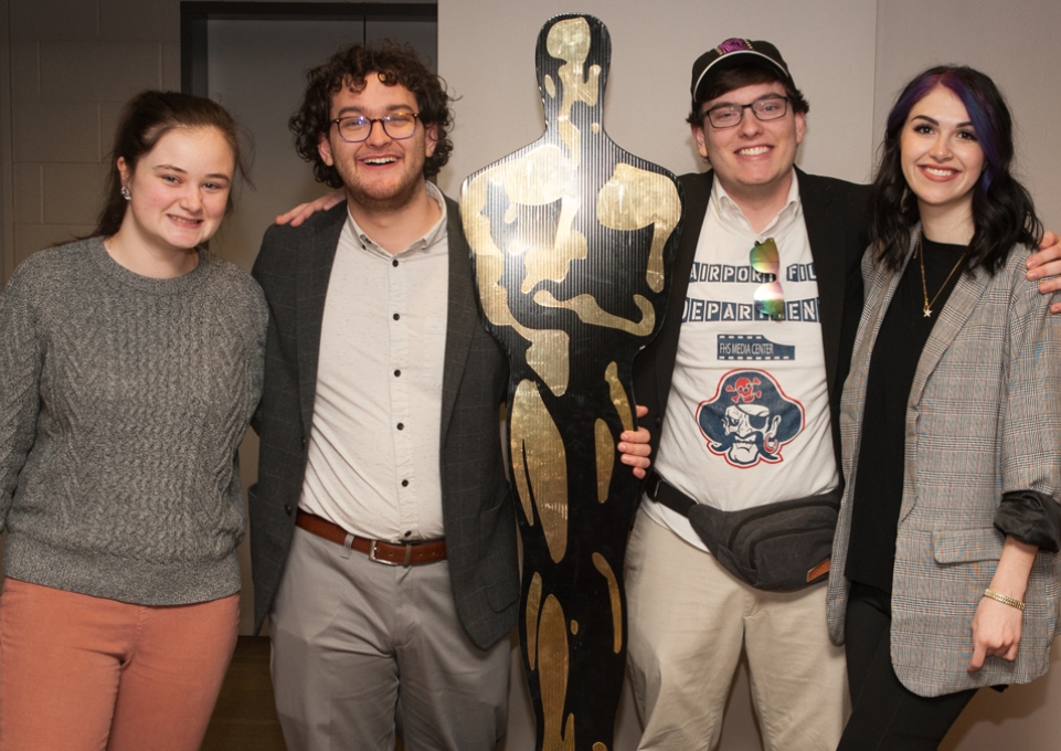 Four students posing with life-size Oscar statue