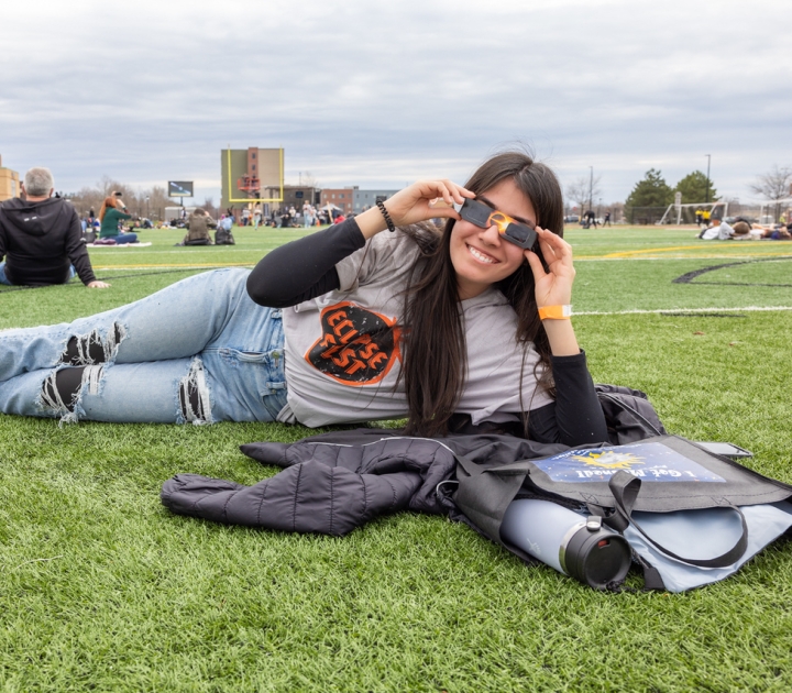 Girl with eclipse glasses on field