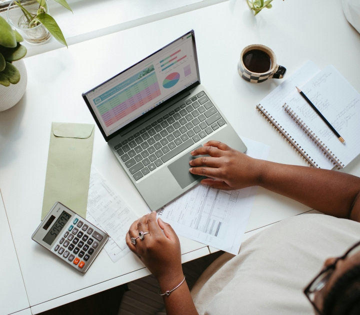 person sitting at desk with computer, calculator, coffee, and notebook