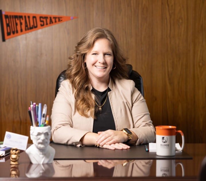 Sarah Bonk sitting at her desk with a Buffalo State pennant and mug in the background