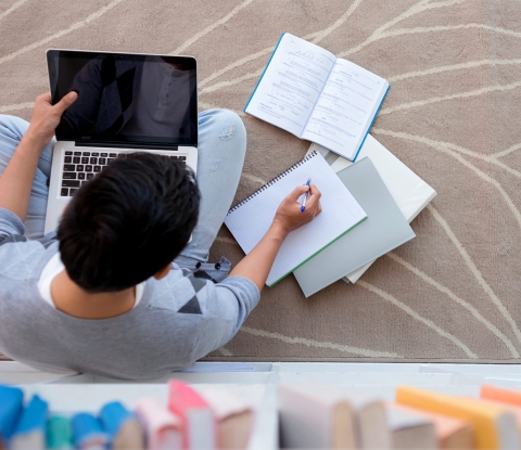 Student sitting on the floor, studying on a laptop