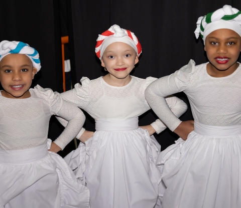 Three young dancers dressed in white with hands on hips  smile for the camera 