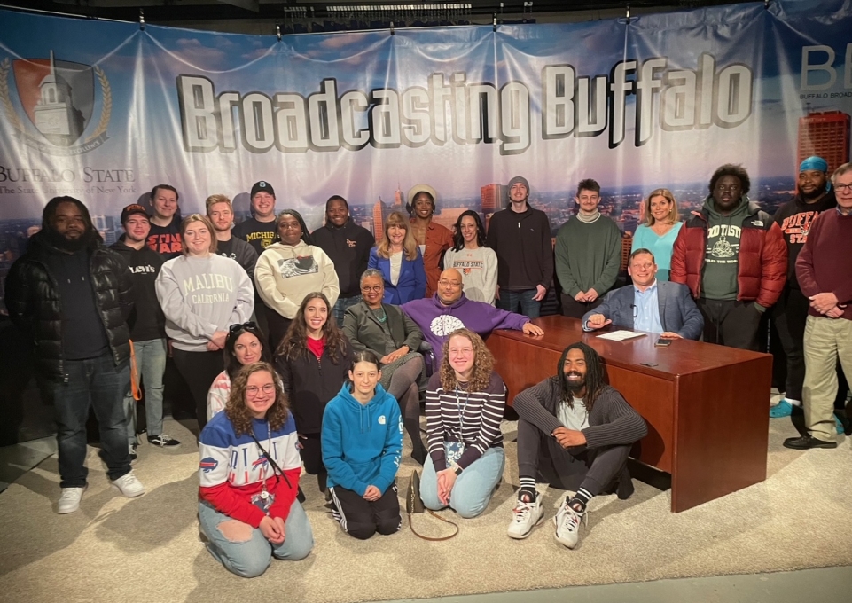 Group of students and professors in front of a sign that reads Broadcasting Buffalo